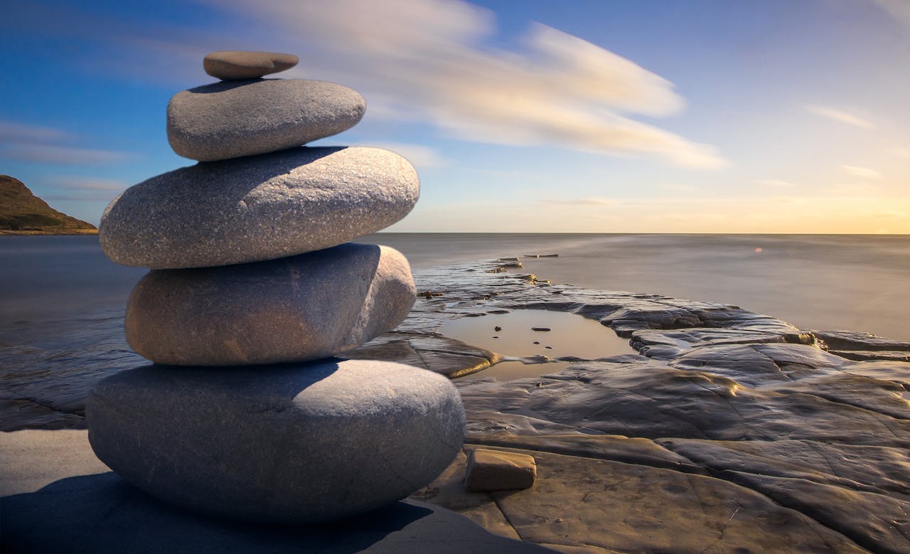 services-03 A serene stack of stones on the rocky seashore during a peaceful sunrise, embodying balance and zen.